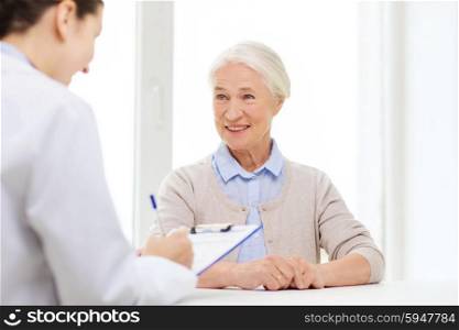 medicine, age, health care and people concept - doctor with clipboard writing prescription for senior woman at hospital