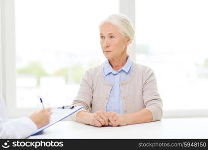 medicine, age, health care and people concept - doctor with clipboard writing prescription for senior woman at hospital