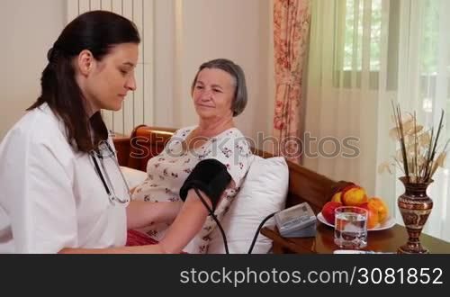 Medicine, age, health care and people concept - doctor with tonometer checking happy senior woman blood pressure level at home. Handheld movement slow motion