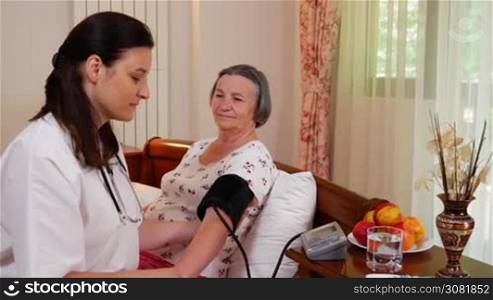 Medicine, age, health care and people concept - doctor with tonometer checking happy senior woman blood pressure level at home. Handheld movement slow motion