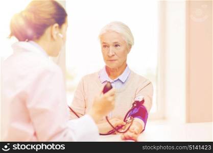 medicine, age, health care and people concept - doctor with tonometer checking senior woman blood pressure level at hospital. doctor with tonometer and senior woman at hospital