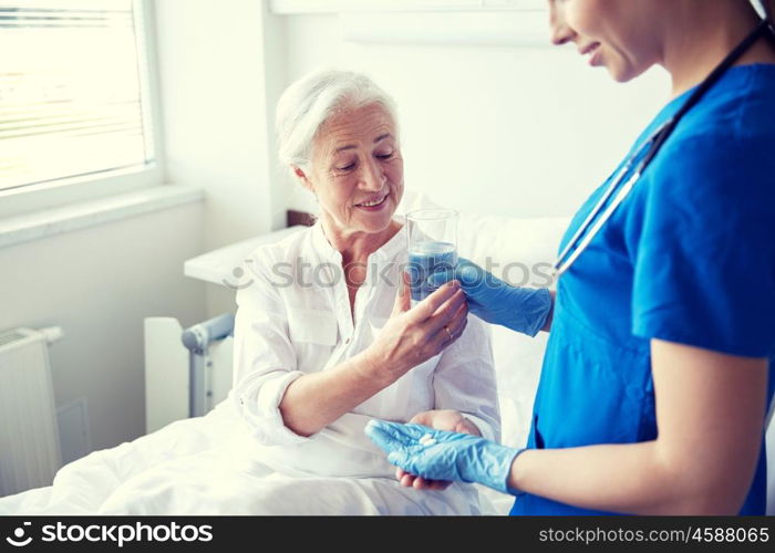 medicine, age, health care and people concept - nurse giving medication and glass of water to senior woman at hospital ward