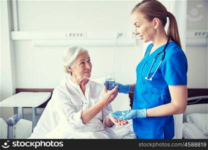 medicine, age, health care and people concept - nurse giving medication and glass of water to senior woman at hospital ward