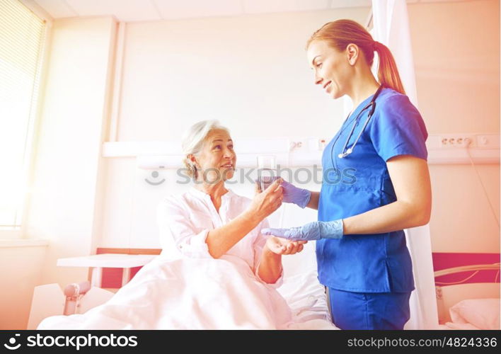 medicine, age, health care and people concept - nurse giving medication and glass of water to senior woman at hospital ward