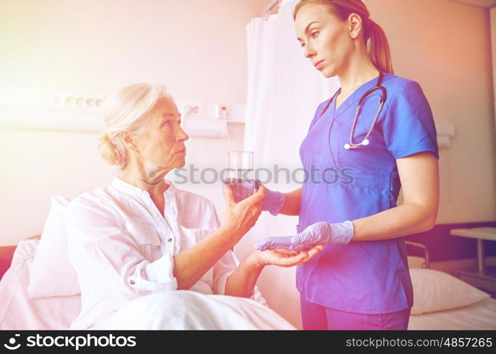 medicine, age, health care and people concept - nurse giving medication and glass of water to senior woman at hospital ward