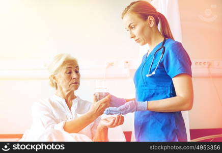 medicine, age, health care and people concept - nurse giving medication and glass of water to senior woman at hospital ward. nurse giving medicine to senior woman at hospital