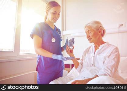 medicine, age, health care and people concept - nurse giving medication and glass of water to senior woman at hospital ward. nurse giving medicine to senior woman at hospital