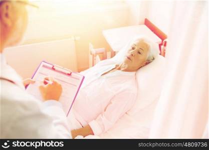 medicine, age, health care and people concept - senior woman and doctor writing to clipboard at hospital ward
