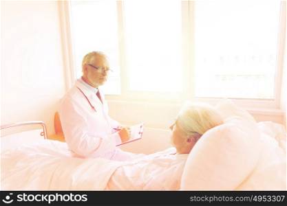 medicine, age, health care and people concept - senior woman and doctor writing to clipboard at hospital ward. senior woman and doctor with clipboard at hospital