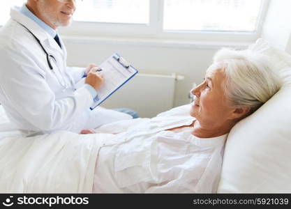 medicine, age, health care and people concept - senior woman and doctor writing to clipboard at hospital ward