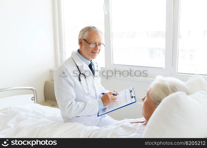 medicine, age, health care and people concept - senior woman and doctor writing to clipboard at hospital ward