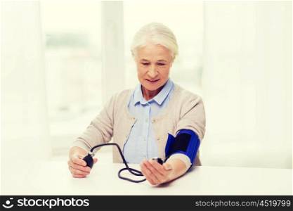medicine, age, health care and people concept - senior woman with tonometer checking blood pressure level at home