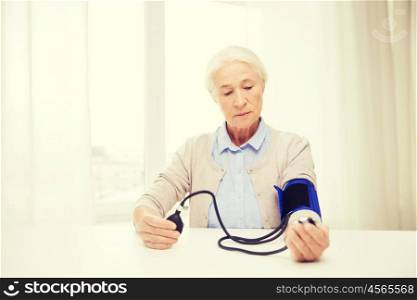 medicine, age, health care and people concept - senior woman with tonometer checking blood pressure level at home