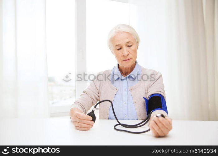 medicine, age, health care and people concept - senior woman with tonometer checking blood pressure level at home