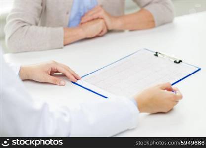 medicine, age, health care, cardiology and people concept - close up of senior woman and doctor hands with cardiogram meeting in medical office