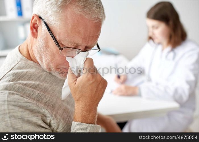 medicine, age, health care, flu and people concept - close up of senior man blowing nose with napkin and doctor at medical office at hospital