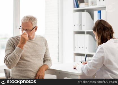 medicine, age, health care, flu and people concept - senior man blowing nose with napkin and doctor with clipboard writing at medical office at hospital