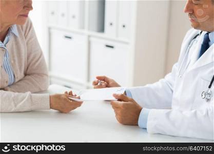 medicine, age, healthcare and people concept - close up of senior woman and doctor with prescription or referral at hospital. woman and doctor with prescription at clinic