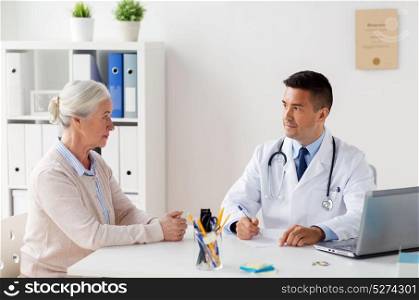 medicine, age, healthcare and people concept - senior woman and doctor with laptop computer writing prescription at hospital. woman and doctor with prescription at clinic