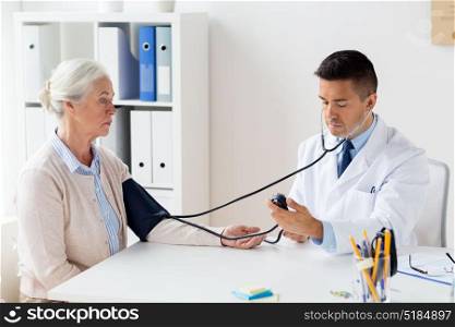 medicine, age, healthcare and people concept - senior woman patient and doctor with tonometer measuring blood pressure at hospital. senior woman and doctor with tonometer at hospital