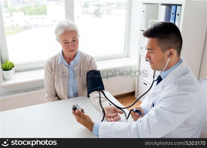 medicine, age, healthcare and people concept - senior woman patient and doctor with tonometer measuring blood pressure at hospital. senior woman and doctor with tonometer at hospital