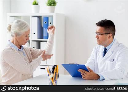 medicine, age, healthcare and people concept - senior woman showing arm to doctor with clipboard at hospital. senior woman and doctor meeting at hospital