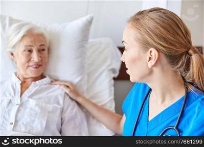 medicine, age, support, health care and people concept - close up of doctor or nurse visiting and cheering senior woman lying in bed at hospital ward. doctor or nurse visiting senior woman at hospital