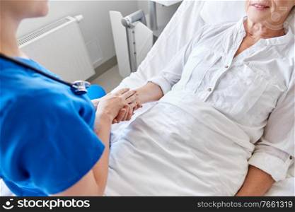 medicine, age, support, health care and people concept - close up of doctor or nurse visiting and cheering senior woman lying in bed at hospital ward. doctor or nurse visiting senior woman at hospital
