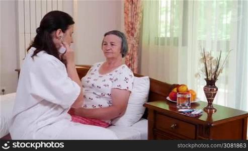 Medicine, age, support, health care and people concept - doctor or nurse with stethoscope visiting senior woman and checking her breath or heartbeat at home. Hand held movement