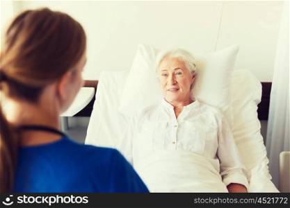 medicine, age, support, health care and people concept - doctor or nurse visiting senior woman lying in bed at hospital ward