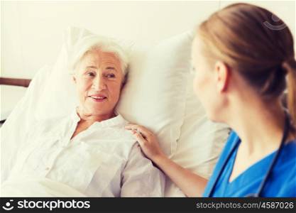 medicine, age, support, health care and people concept - doctor or nurse visiting and cheering senior woman lying in bed at hospital ward