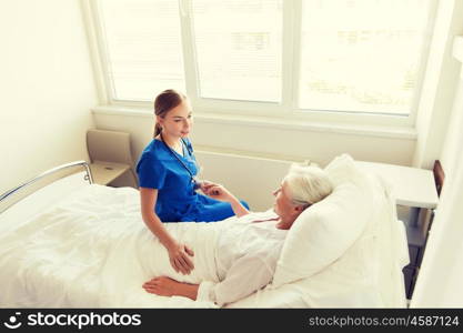 medicine, age, support, health care and people concept - doctor or nurse visiting and cheering senior woman lying in bed at hospital ward