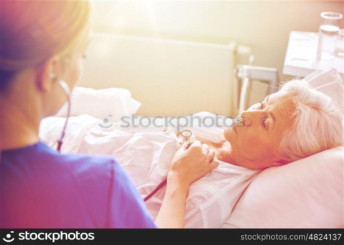 medicine, age, support, health care and people concept - doctor or nurse with stethoscope visiting senior woman and checking her breath or heartbeat at hospital ward