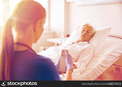 medicine, age, support, health care and people concept - doctor or nurse adjusting bed with remote control for senior woman patient at hospital ward