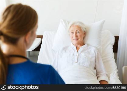 medicine, age, support, health care and people concept - doctor or nurse visiting senior woman lying in bed at hospital ward