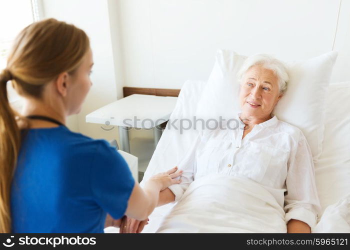 medicine, age, support, health care and people concept - doctor or nurse visiting and cheering senior woman lying in bed at hospital ward