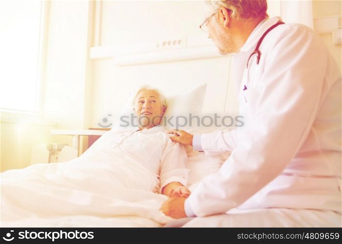 medicine, age, support, health care and people concept - doctor visiting and cheering senior woman lying in bed at hospital ward