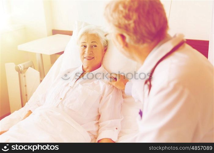 medicine, age, support, health care and people concept - doctor visiting and cheering senior woman lying in bed at hospital ward