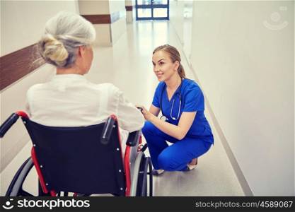 medicine, age, support, health care and people concept - happy nurse talking to senior woman patient in wheelchair at hospital corridor