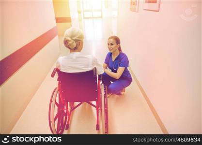 medicine, age, support, health care and people concept - happy nurse talking to senior woman patient in wheelchair at hospital corridor