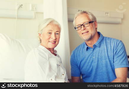 medicine, age, support, health care and people concept - happy senior man visiting and cheering his woman lying in bed at hospital ward