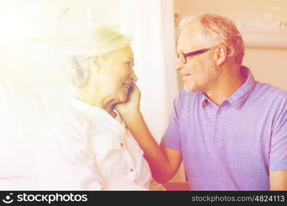 medicine, age, support, health care and people concept - happy senior man visiting and cheering his woman lying in bed at hospital ward