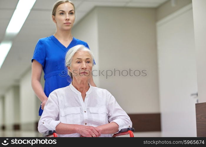 medicine, age, support, health care and people concept - nurse taking senior woman patient in wheelchair at hospital corridor