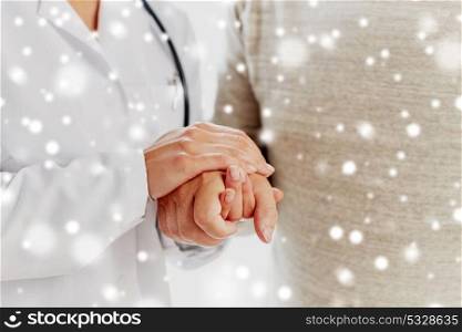 medicine, age, support, healthcare and people concept - close up of doctor or nurse holding senior man hand at hospital over snow. close up of doctor holding old man hand