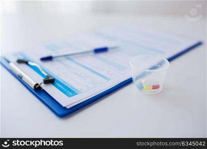 medicine and healthcare concept - clipboard with report and drugs in medical cup. clipboard with report and drugs in medical cup