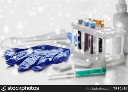 medicine and healthcare concept - close up of beakers with blood test in holder, syringe, mask, wound wipes and gloves at laboratory in winter over snow. beakers with blood tests, syringe, gloves and mask