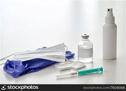 medicine and healthcare concept - close up of syringe, drug, wound wipes, hand sanitizer with gloves and mask on table. syringe, medicine, wound wipes, gloves and mask