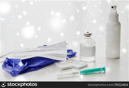 medicine and healthcare concept - close up of syringe, drug, wound wipes, hand sanitizer with gloves and mask on table in winter over snow. syringe, medicine, wound wipes, gloves and mask