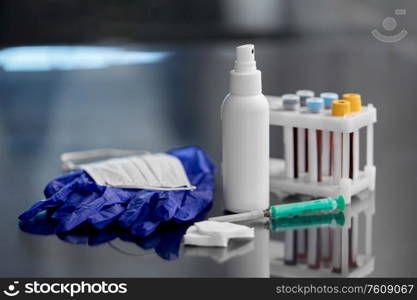 medicine and healthcare concept - close up of syringe, hand sanitizer, beakers with blood test in holder, and mask with wound wipes and gloves at laboratory. syringe, beakers with blood test, gloves and mask