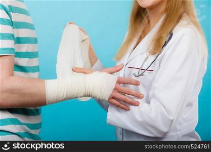 Medicine and healthcare. Female doctor bandaging male hand sprained wrist. Young man visiting medical professionalist.. Doctor bandaging sprained wrist.